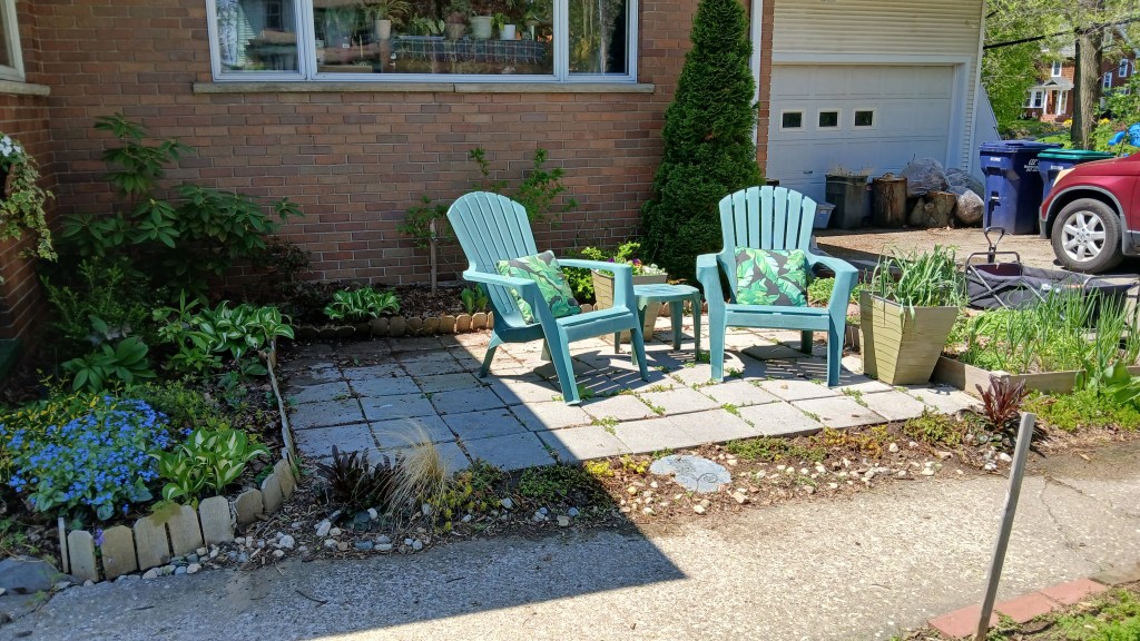 The front patio display two Adirondack chairs and is surrounded by gardens
