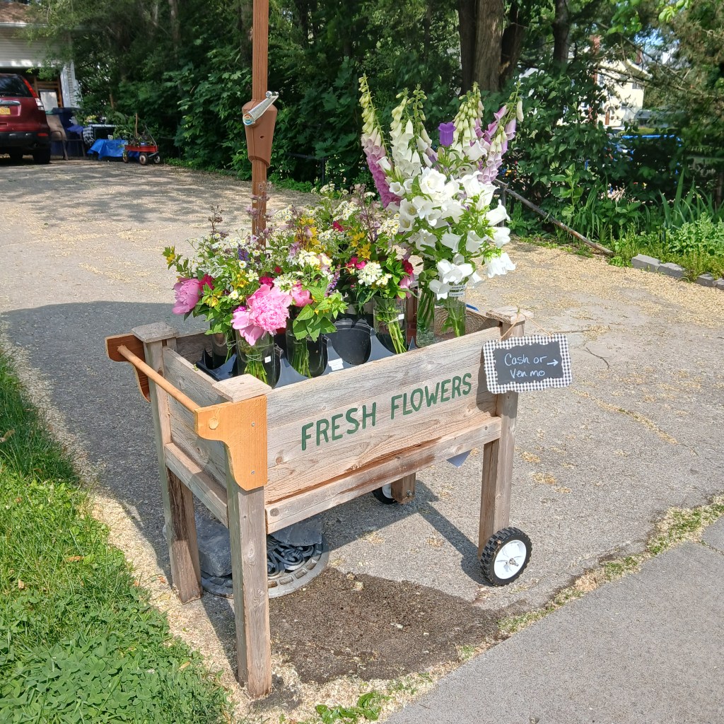 A flower cart filled with bouquets for sale at the end of a driveway